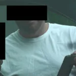 A man with black eyes and no shirt is holding a cell phone.