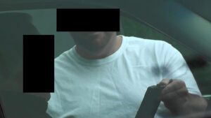 A man with black eyes and no shirt is holding a cell phone.