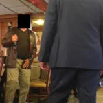 A man in brown jacket and pants standing next to another man.