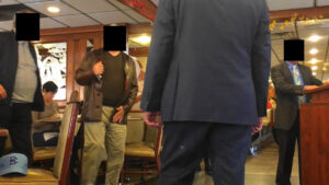 A man in brown jacket and pants standing next to another man.