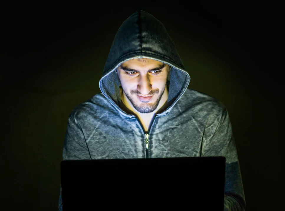 A man in a hooded jacket looking at his laptop.